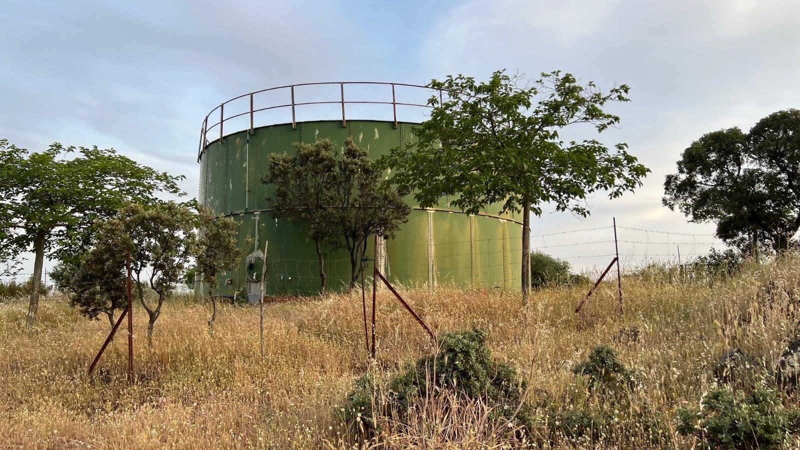 Depósito de agua metálico entre árboles y pasto seco